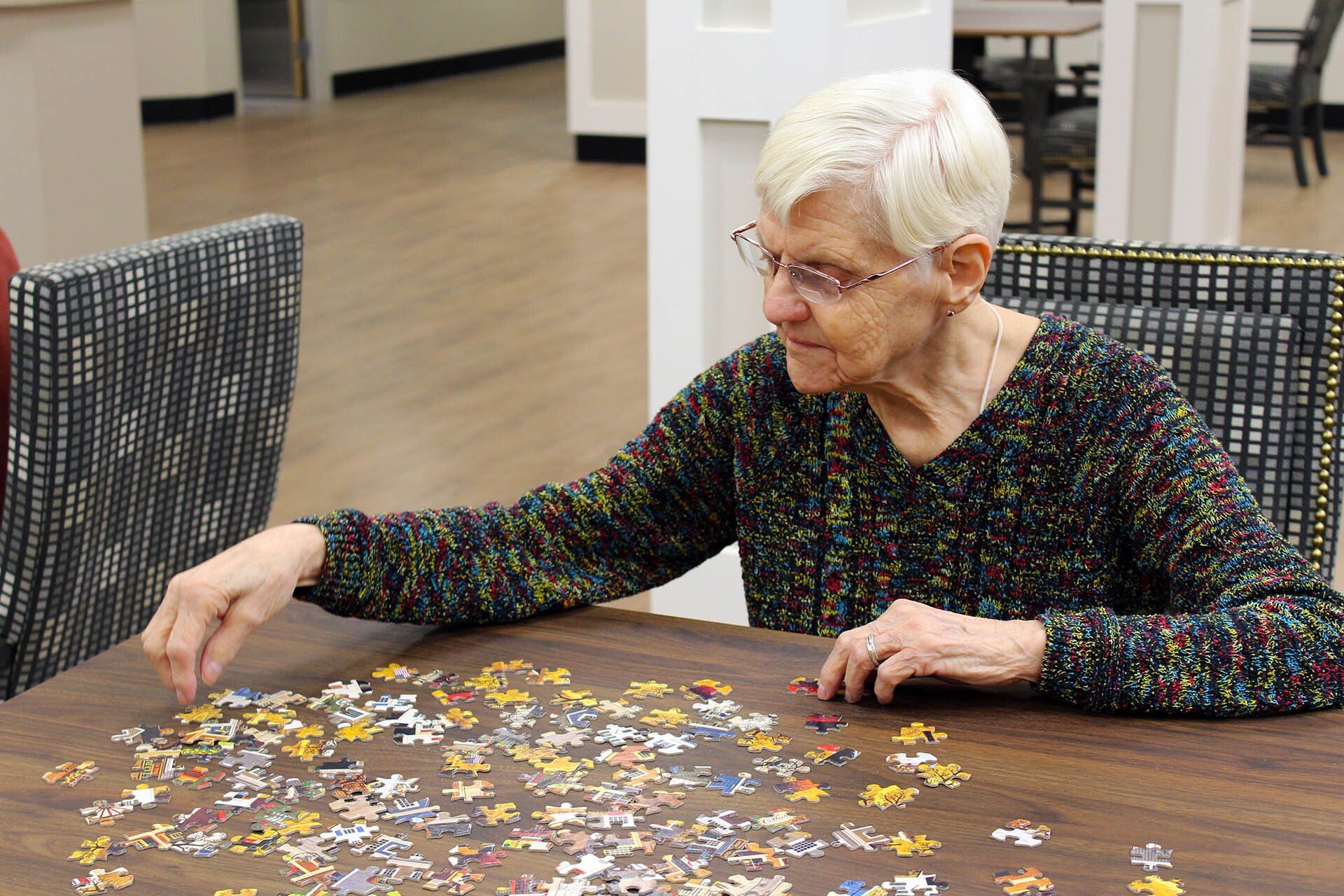 An elderly woman is sitting at a table playing a puzzle.
