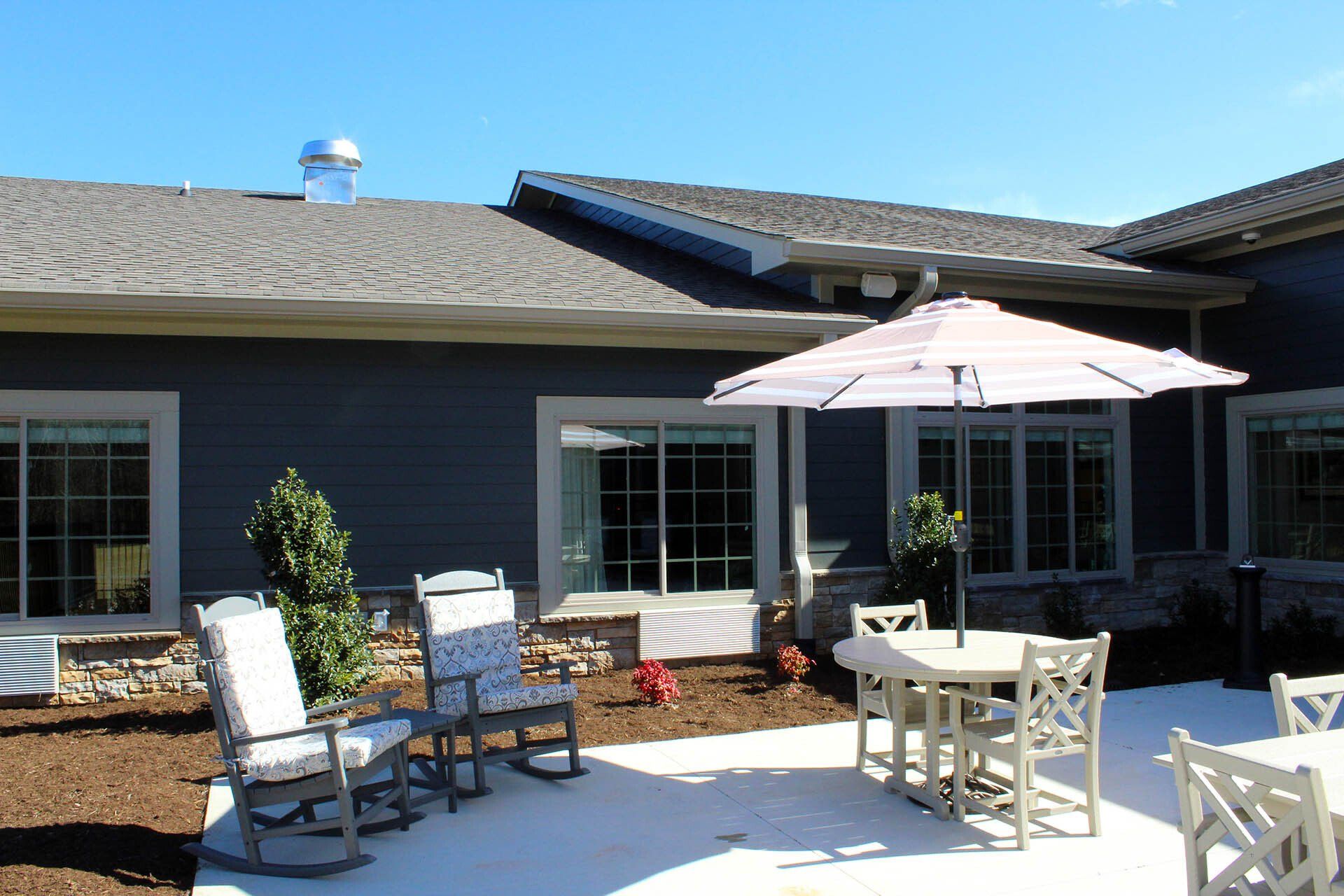 A patio with rocking chairs tables and umbrellas in front of a house