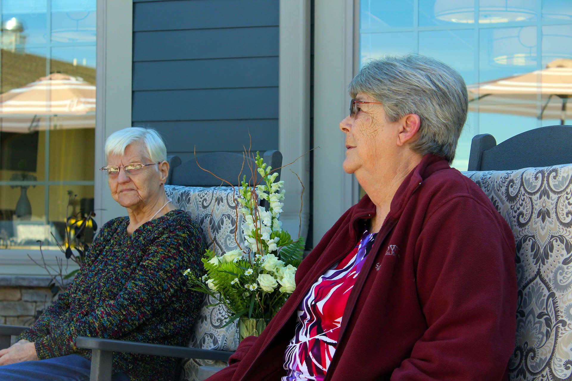 Two older women are sitting in chairs on a porch.