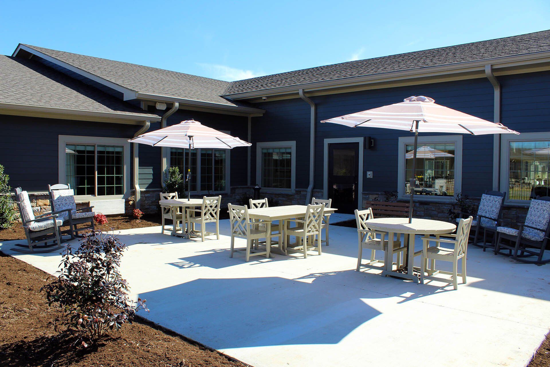 A patio with tables and chairs and umbrellas in front of a house.