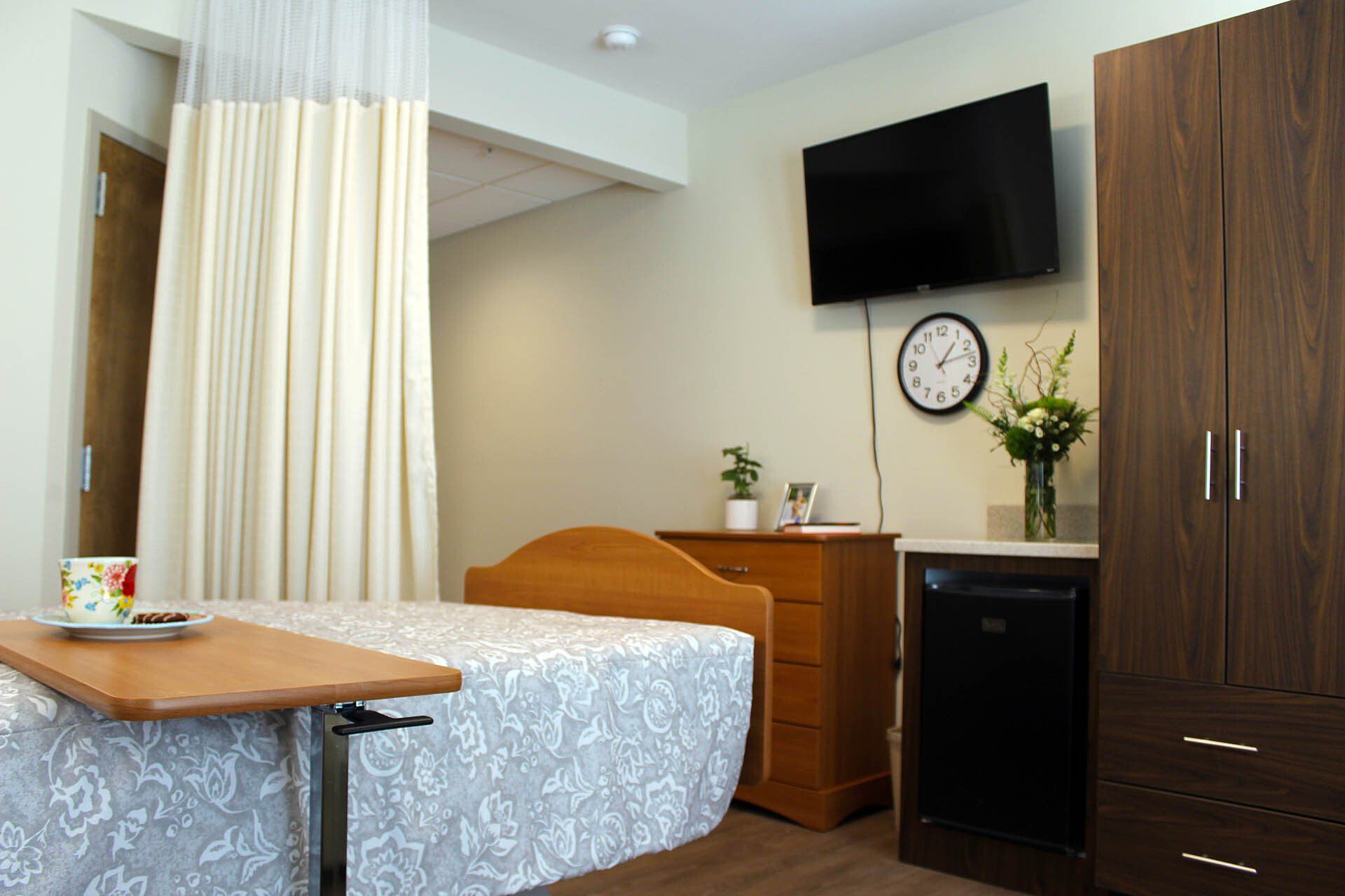 A hospital room with a bed , dresser , clock and television.