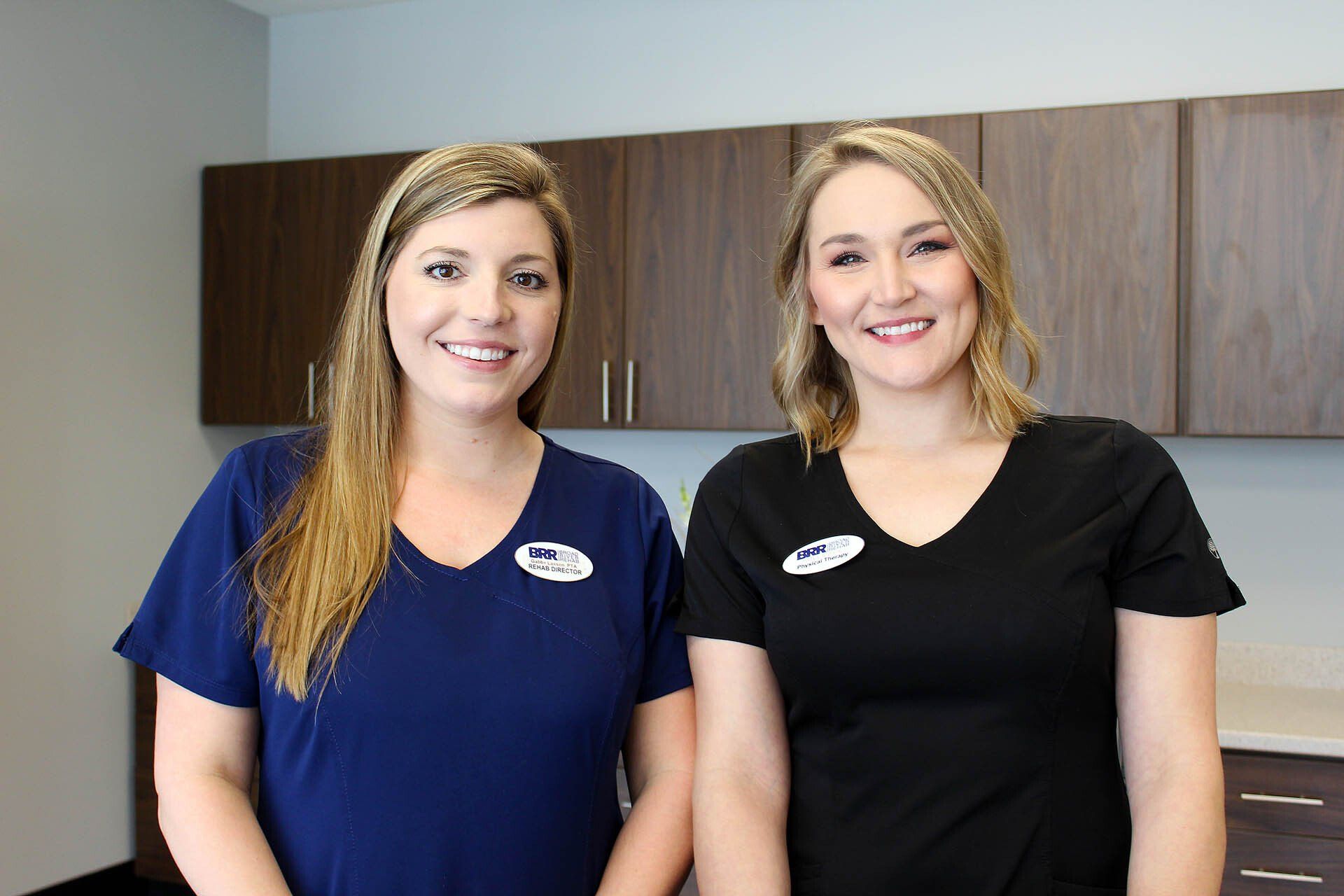 Two women in scrubs are standing next to each other and smiling.
