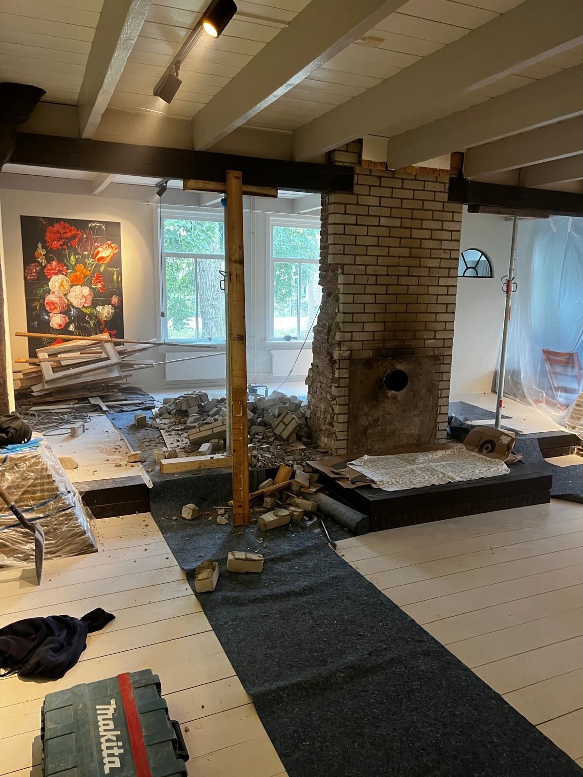 Een kamer met een schilderij aan de muur en een bakstenen schoorsteen die wordt gesloopt.