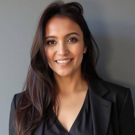 A woman with long hair is wearing a black jacket and smiling.