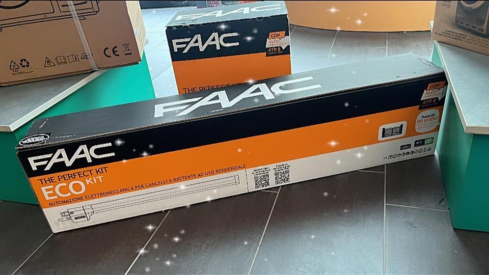 Scatole di prodotti FAAC per l'automazione dei cancelli su un pavimento in legno con alcune piattaforme verdi. Sulla lunga scatola c'è la scritta 