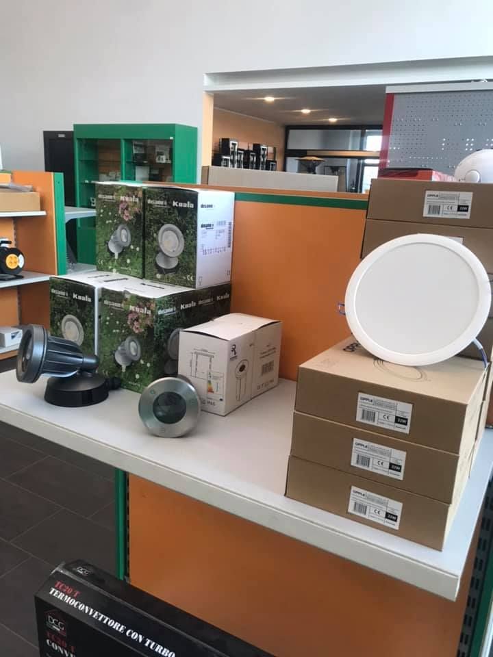Esposizione di apparecchi di illuminazione, tra cui faretti e faretti da incasso a soffitto, sul bancone di un negozio. Sono visibili scatole e campioni.