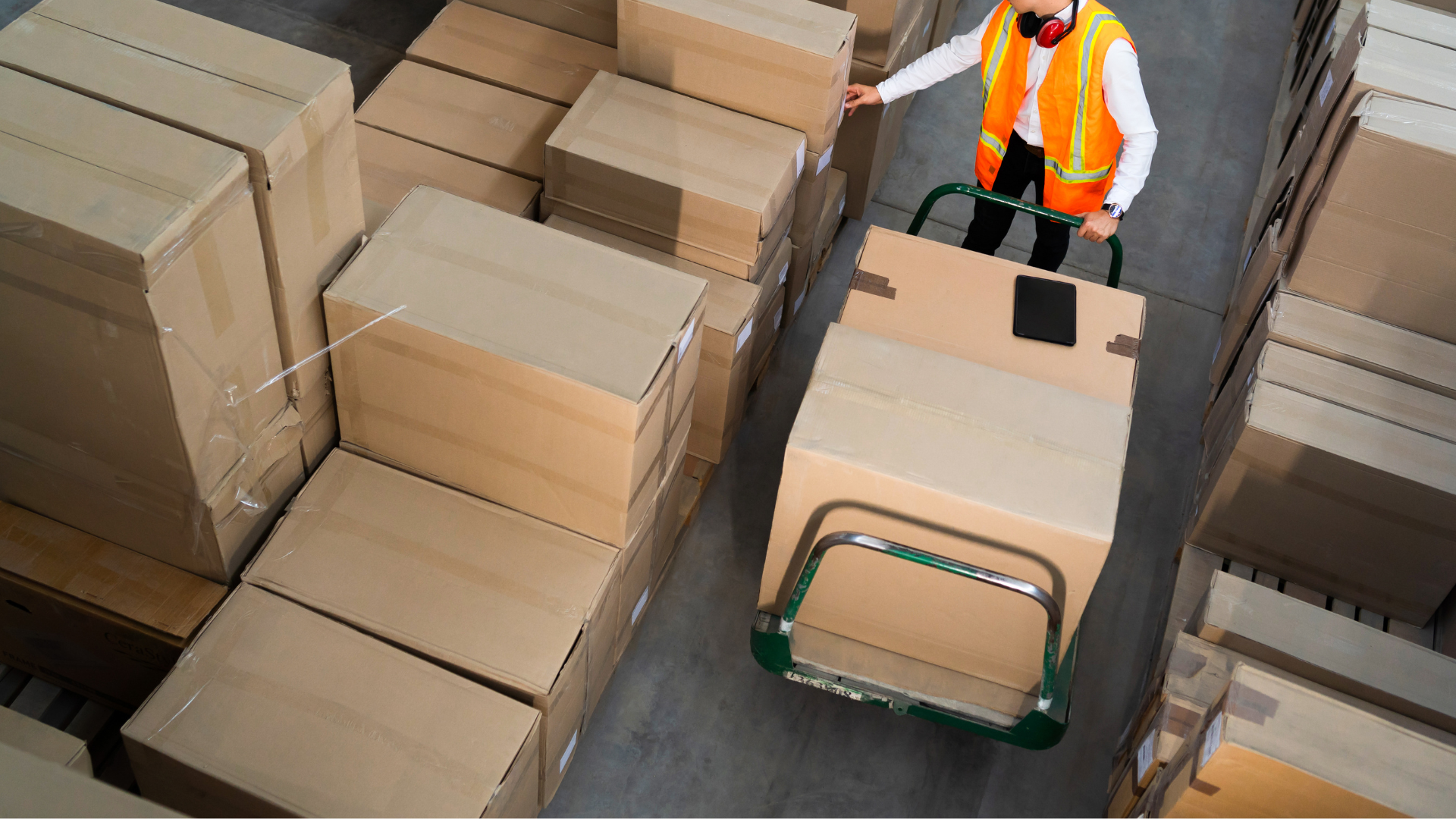A man is pushing a cart full of boxes in a warehouse.