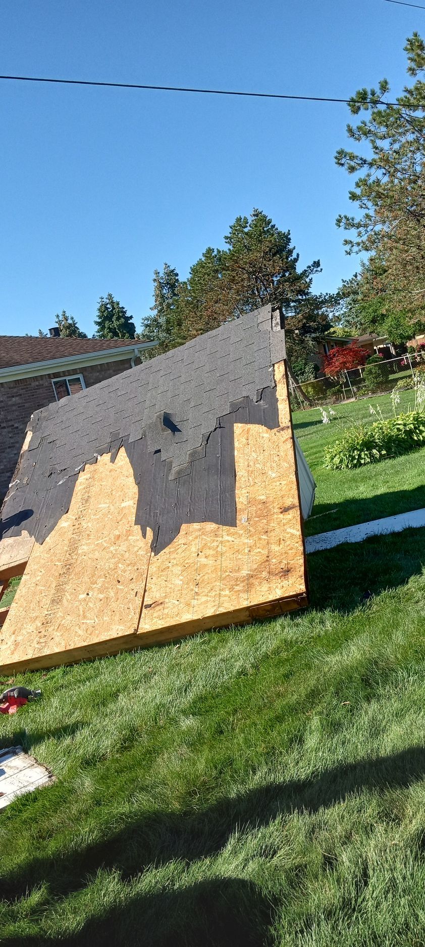 A large piece of wood is sitting in the grass next to a roof.