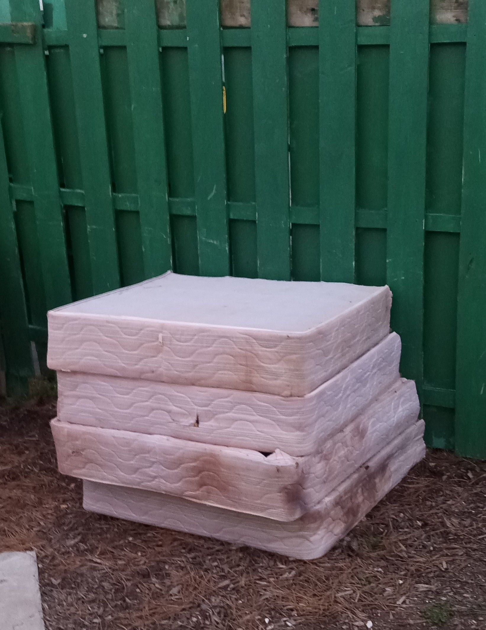 A stack of mattresses is sitting in front of a green fence.
