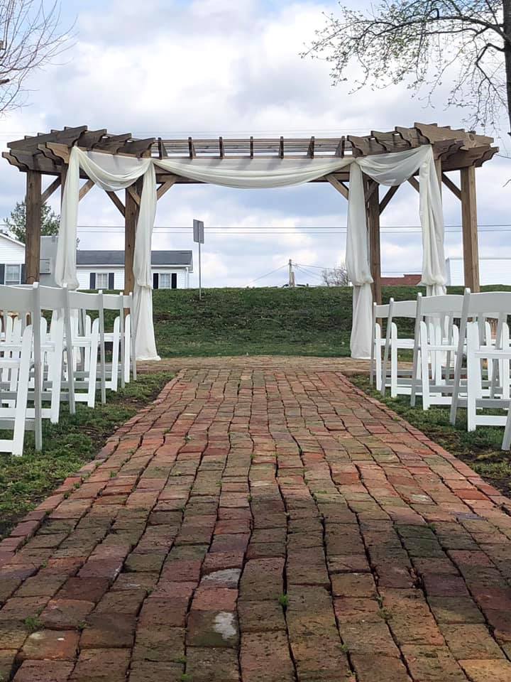 A brick walkway leading to a pergola with white chairs.