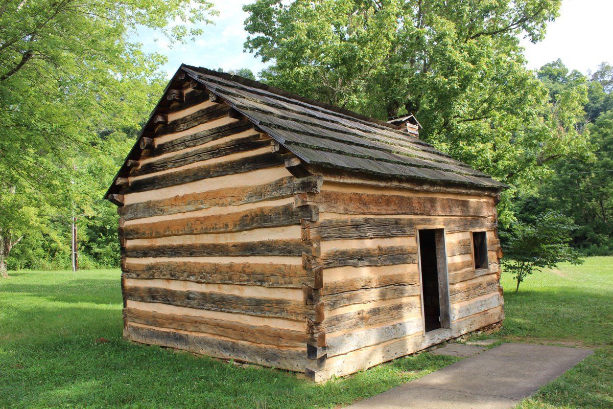 A small log cabin is sitting in the middle of a grassy field.