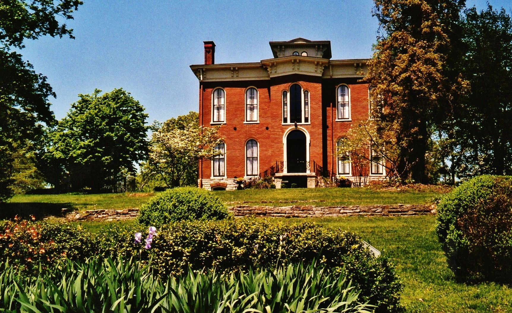A large brick house sits in the middle of a lush green field