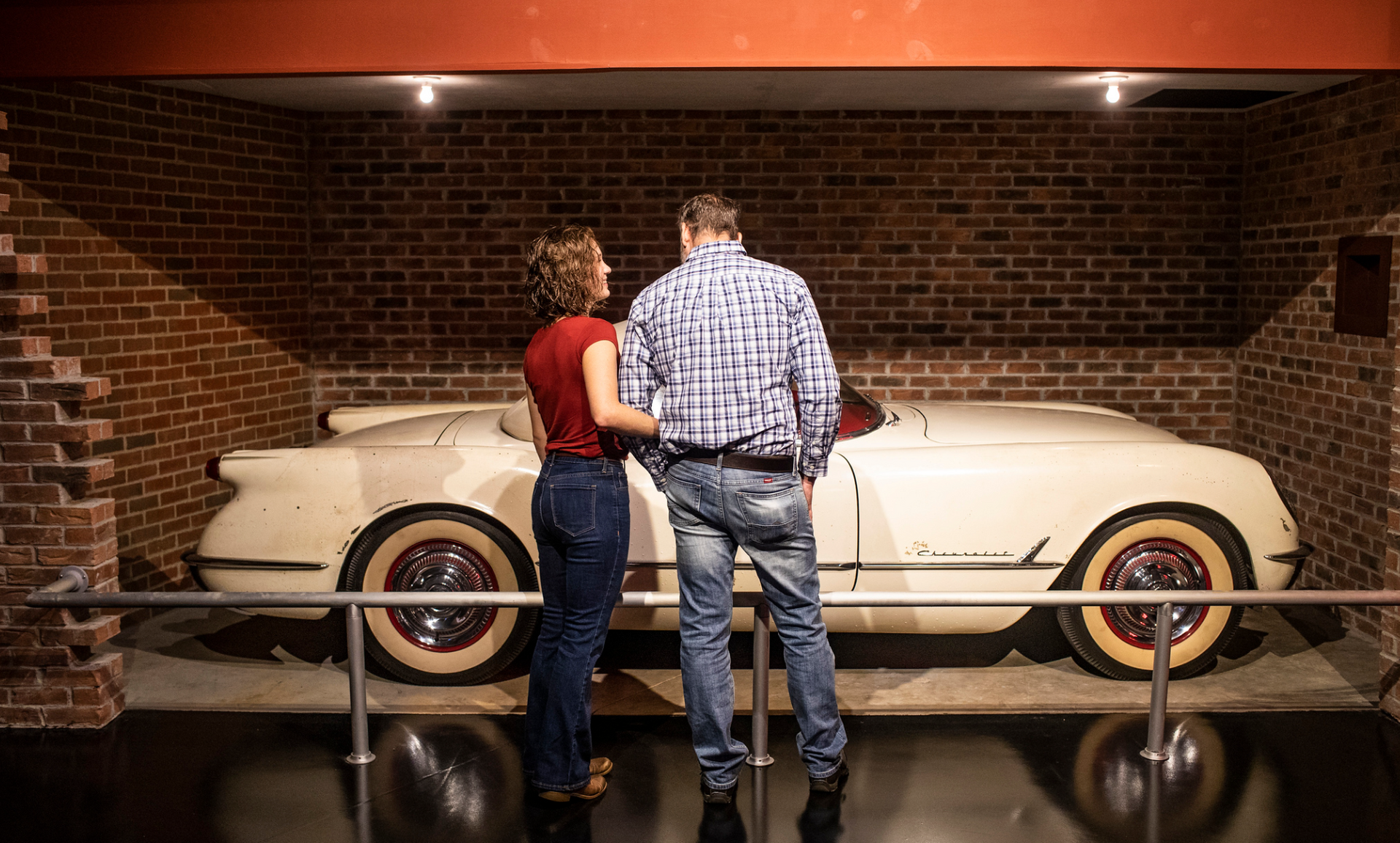 A man and a woman are looking at a white car in a garage.