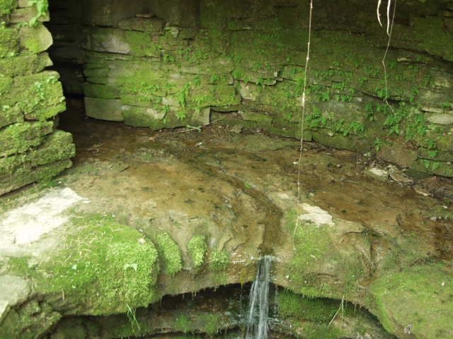 A small waterfall in a cave surrounded by moss covered rocks.