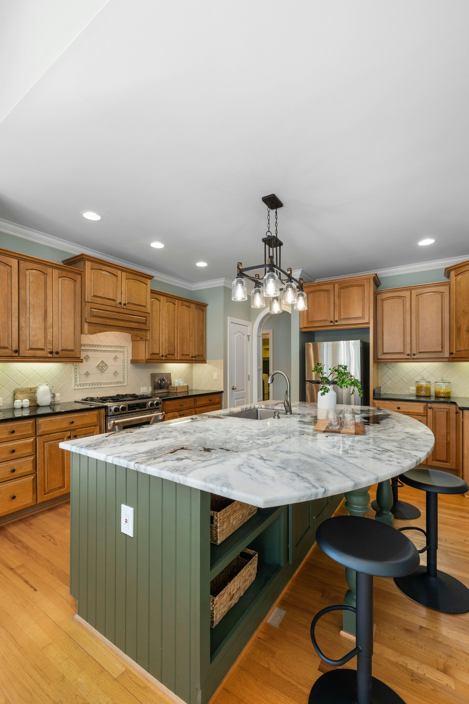 Spacious kitchen with wood cabinets, marble island, hanging lights, and bar stools