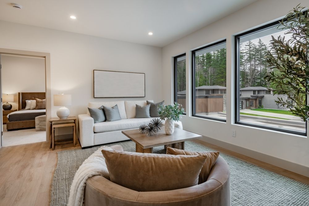 Bright modern living room with sofa, chair, coffee table, and large windows overlooking a yard