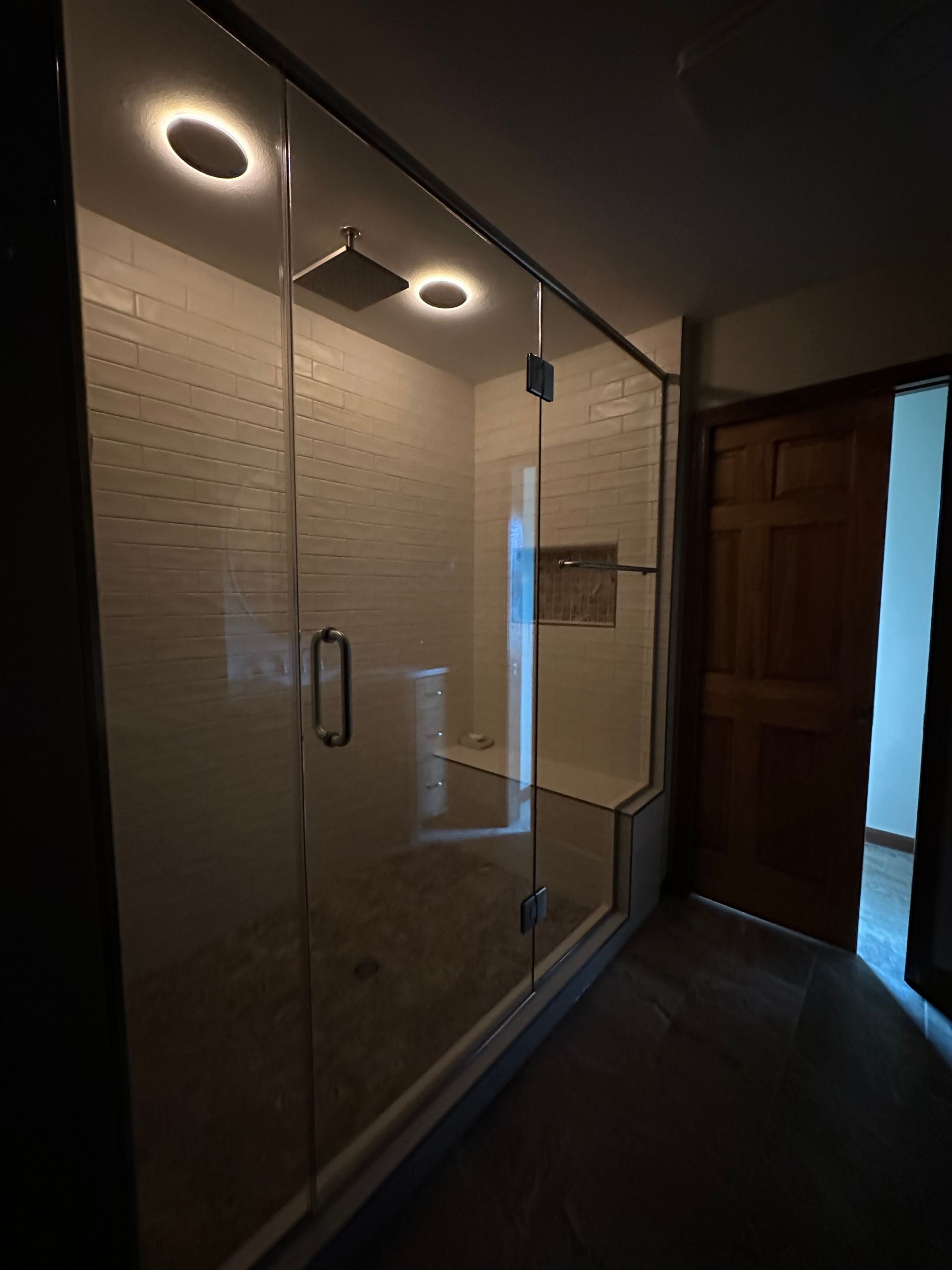 Glass shower enclosure with two lit circular ceiling lights in a dim bathroom