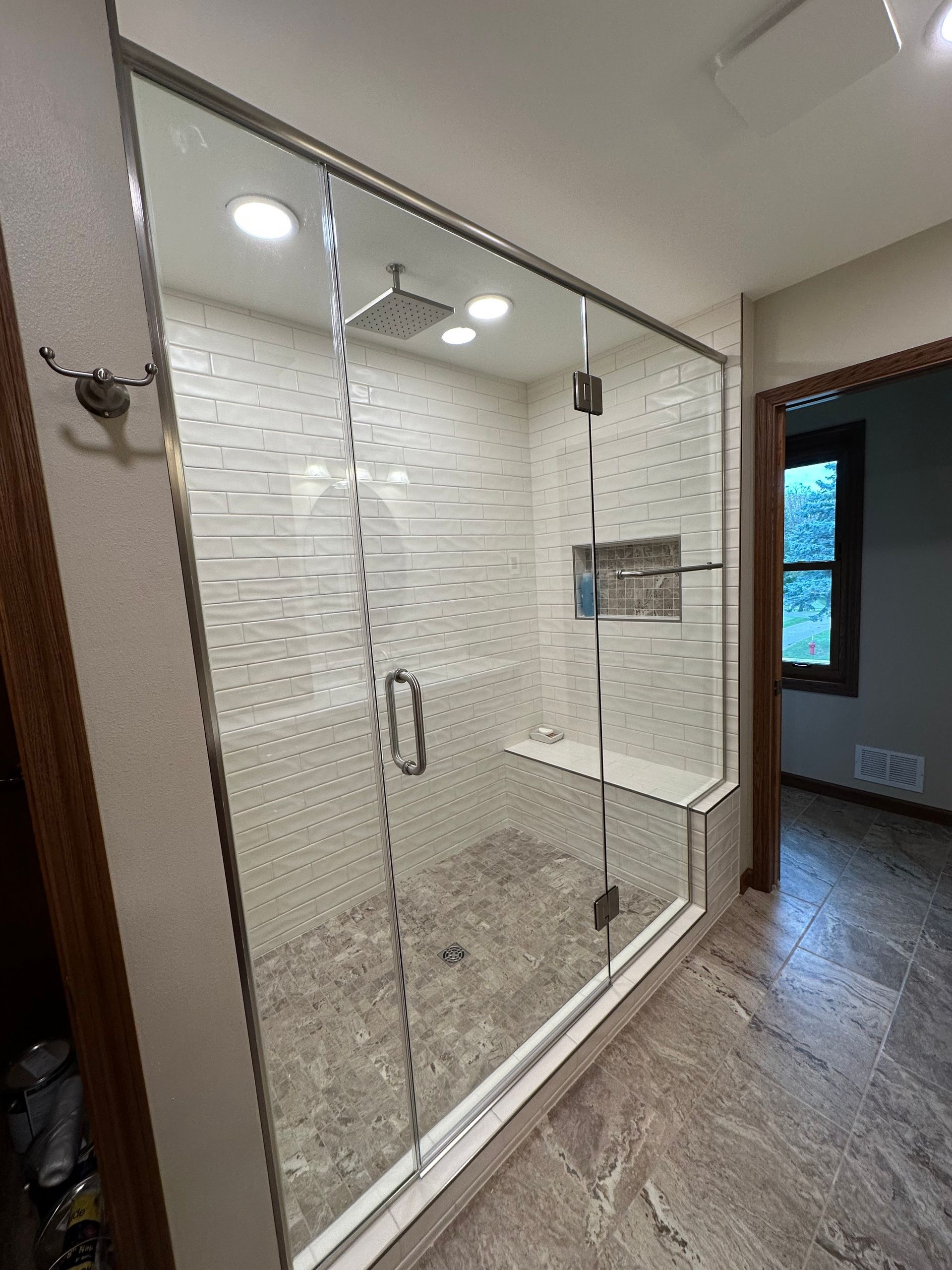 Glass shower enclosure in a tiled bathroom with a chrome handle and a small shelf.