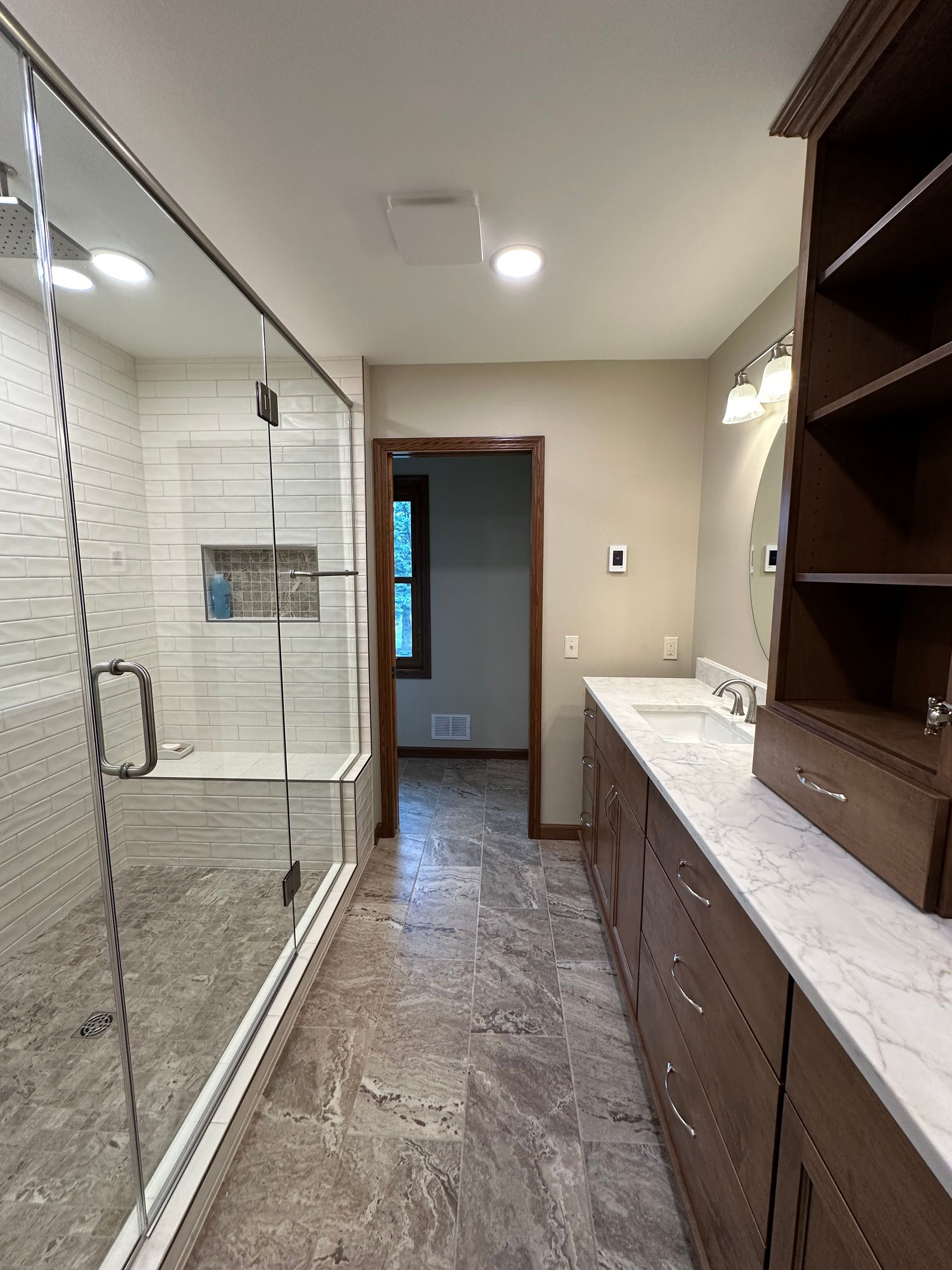 Modern bathroom with glass shower, double vanity, and doorway to adjoining room.