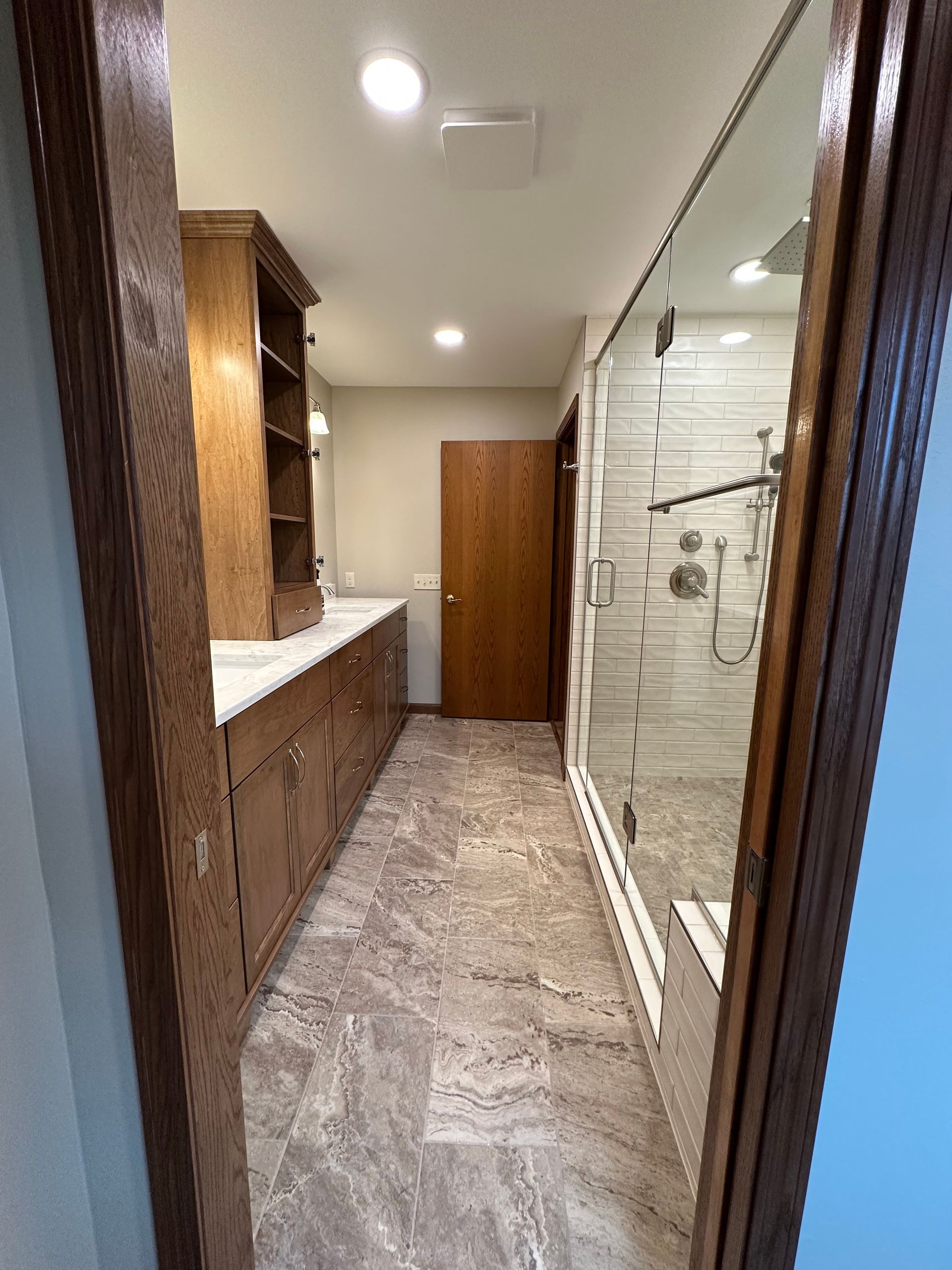 Long narrow bathroom with wood cabinets, white countertop, and glass shower enclosure.