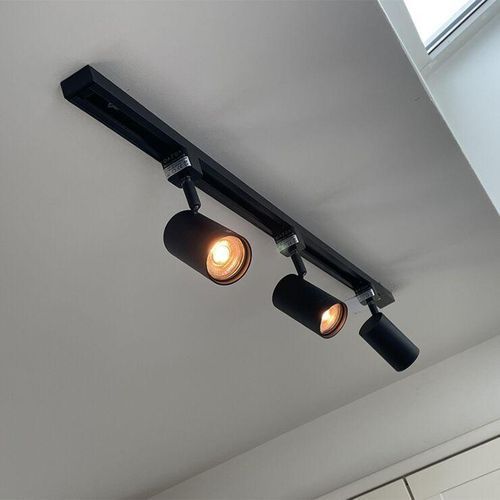 Black ceiling track light with three adjustable spotlights in a white room