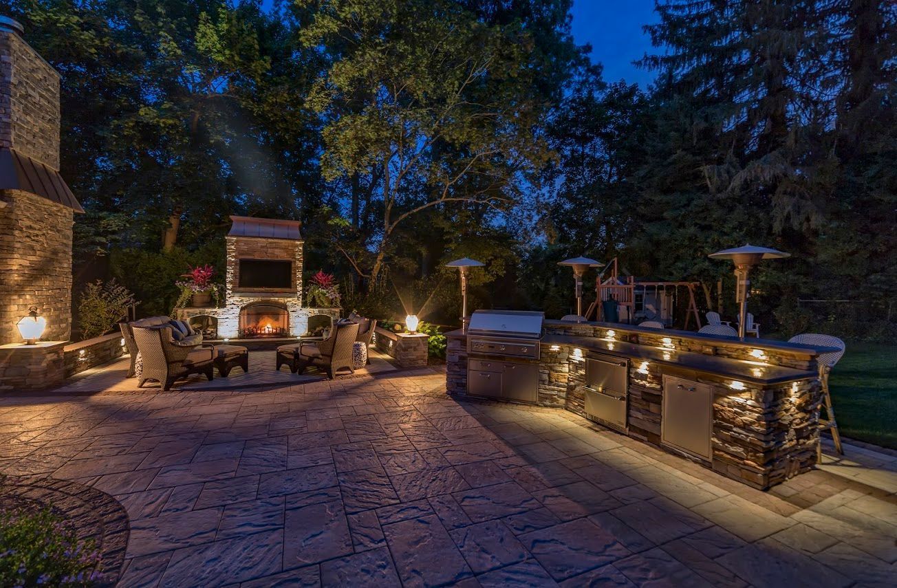 Stone patio with outdoor kitchen and grill lighting a nighttime backyard gathering area