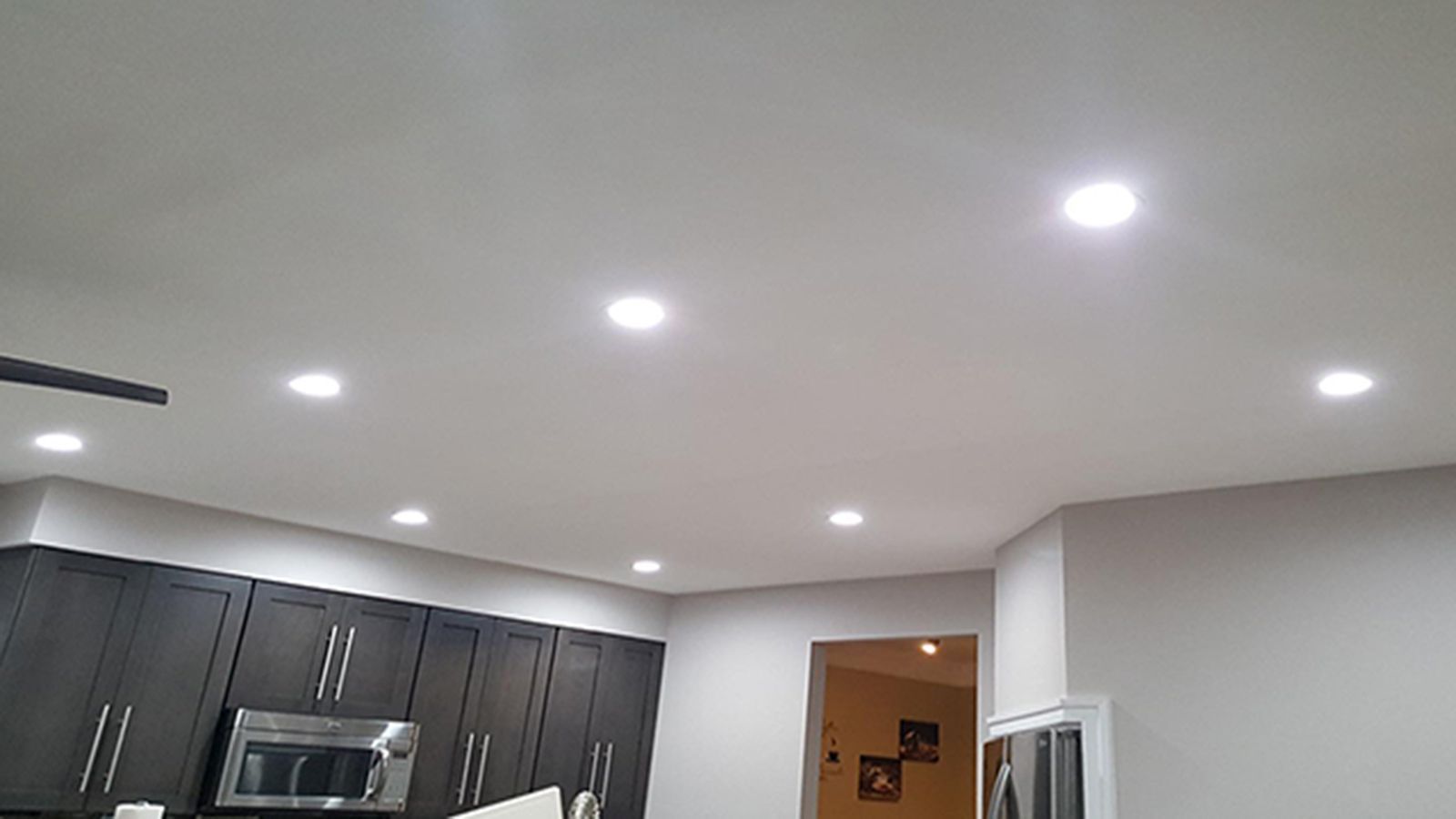 Modern kitchen ceiling with recessed lights, dark cabinets, and an open doorway to another room