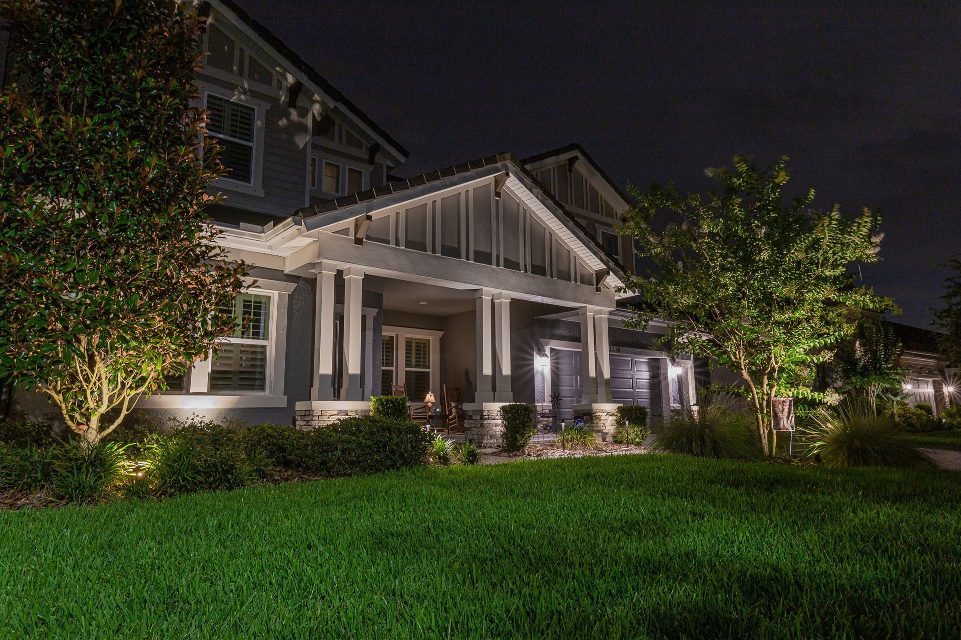 Well-lit suburban house at night with a green lawn and trees