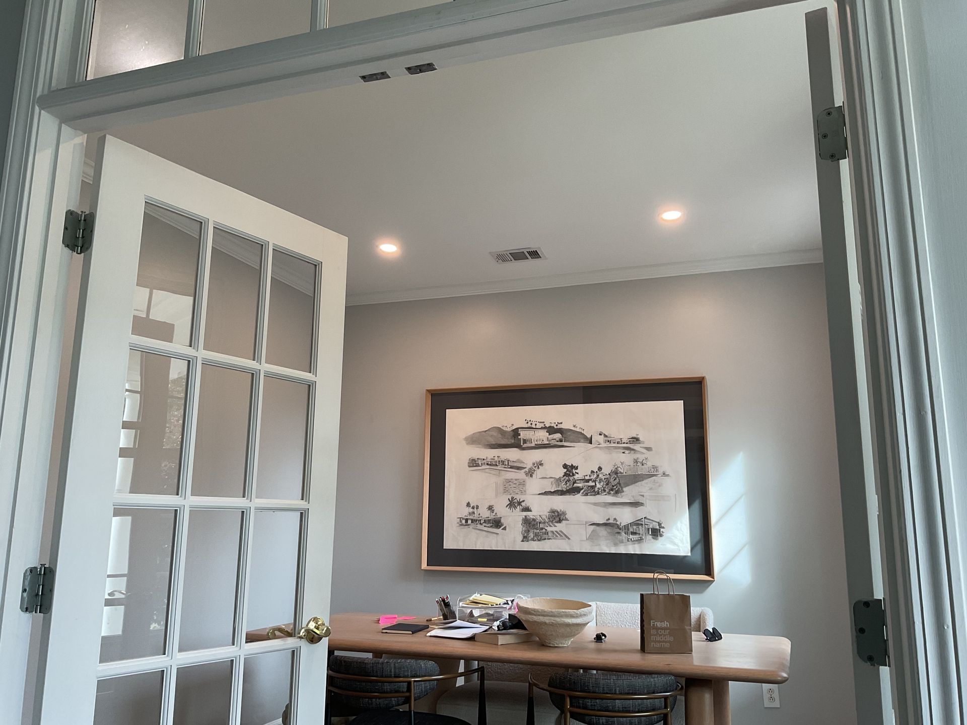 Open French doors to a gray dining room with a wood table and framed wall art.