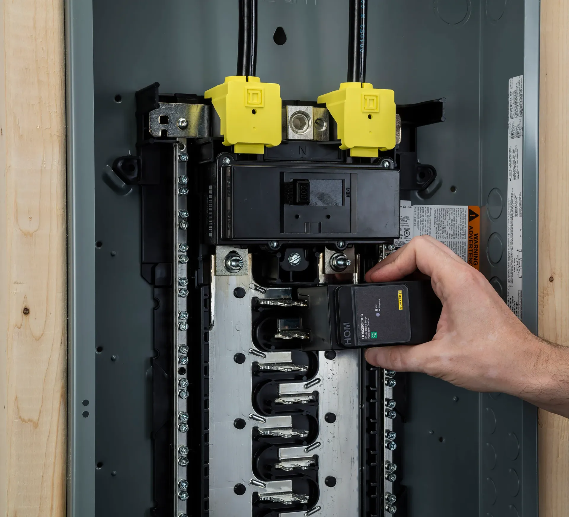 Hand placing a black breaker into an electrical panel with yellow main switches