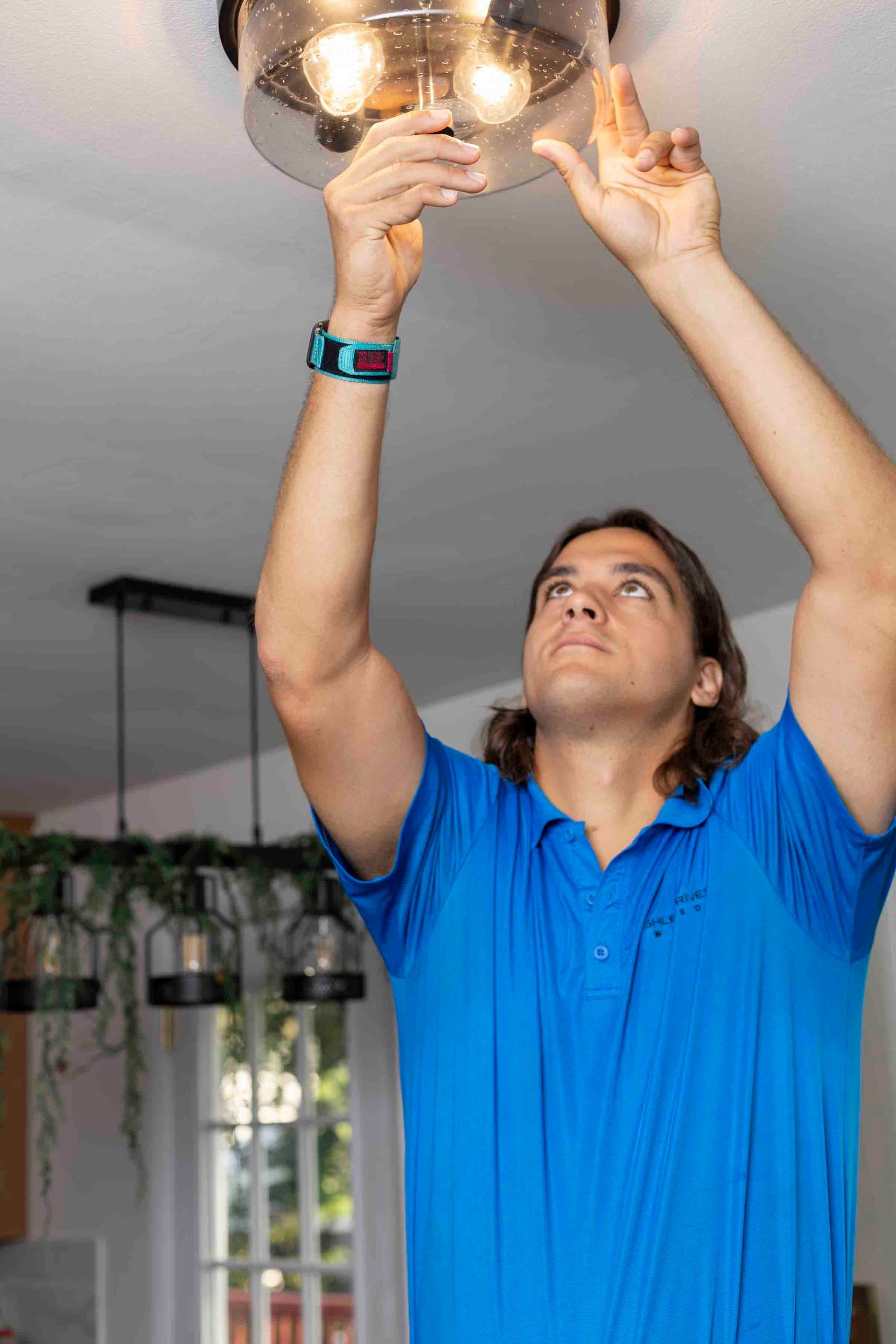 Man in blue shirt adjusting a ceiling light fixture indoors