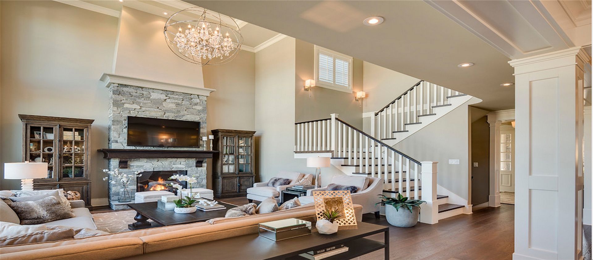 Bright living room with fireplace, chandelier, sofas, and staircase in a spacious open interior