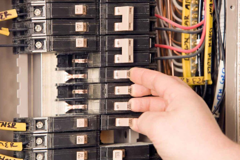 Hand checking circuit breakers in an electrical panel with tangled wires nearby