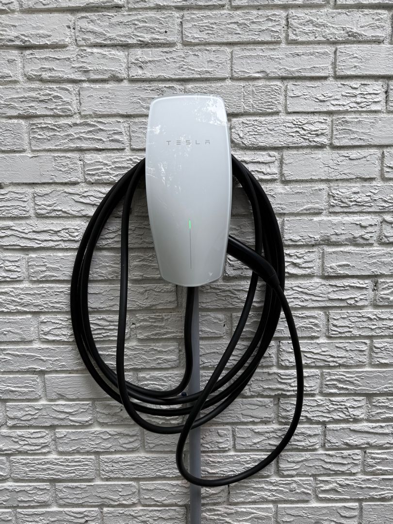 White wall-mounted EV charger with black coiled cable against a gray brick wall