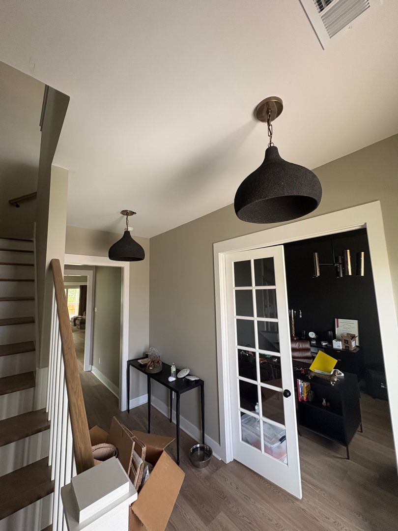 Hallway with open French doors, black pendant lights, stairs, and an unpacked room in the background