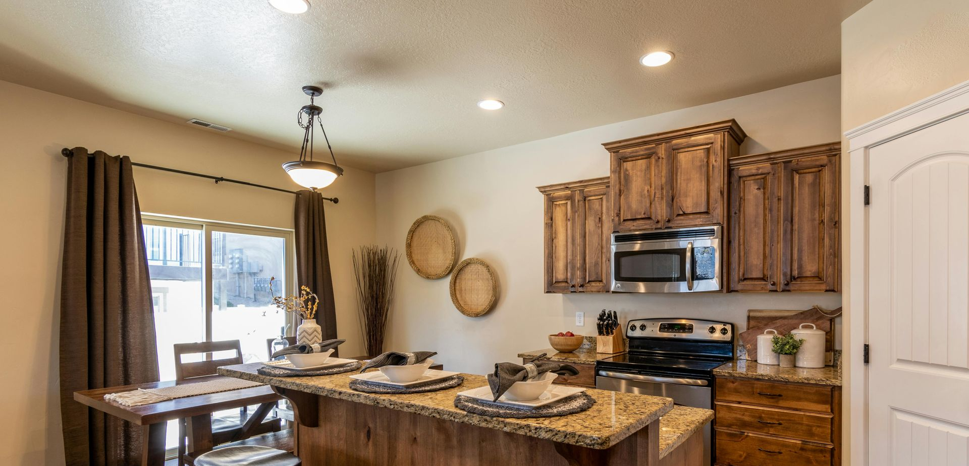 Bright kitchen and dining area with granite island, wooden cabinets, and a window with curtains