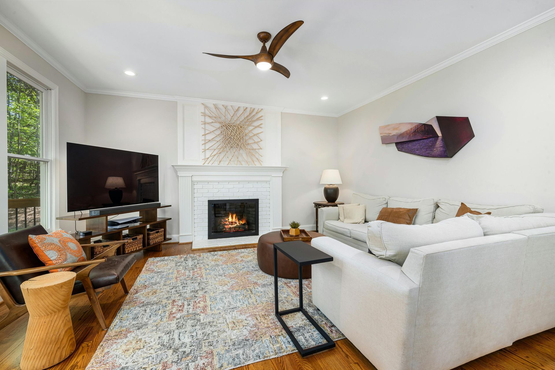 Bright living room with white sectional, fireplace, TV, patterned rug, and large windows
