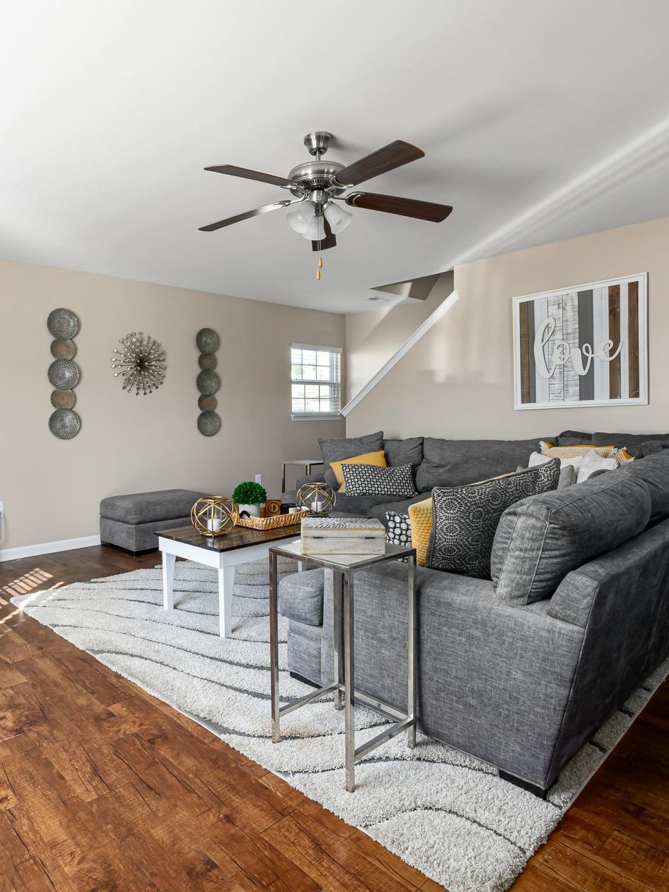 Modern living room with gray sectional, white rug, wood floor, coffee table, and ceiling fan