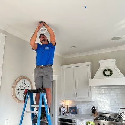 Man on a ladder adjusting a ceiling fixture in a bright kitchen