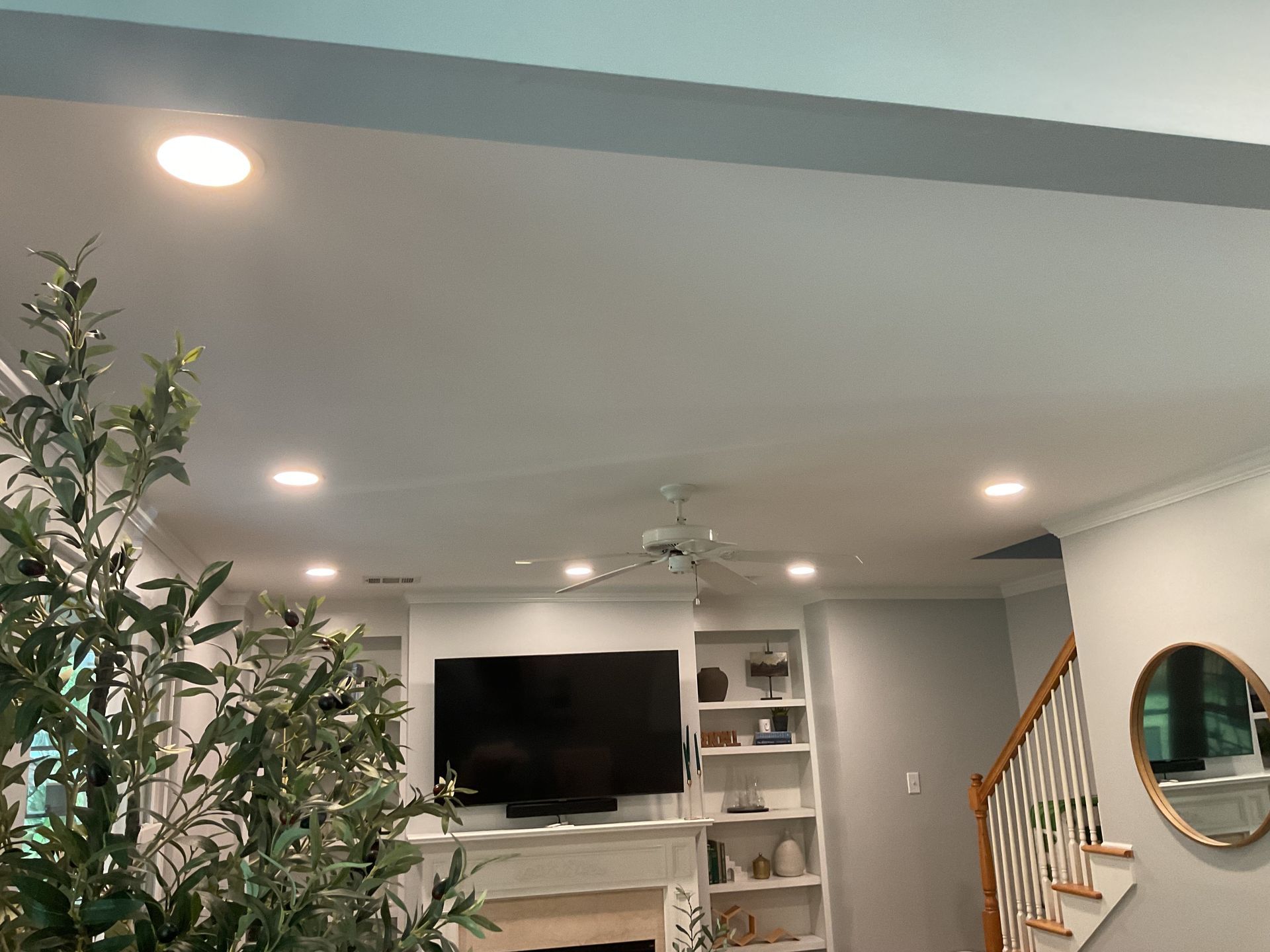 Bright living room with recessed lights, wall-mounted TV, built-in shelves, and staircase with wood railing