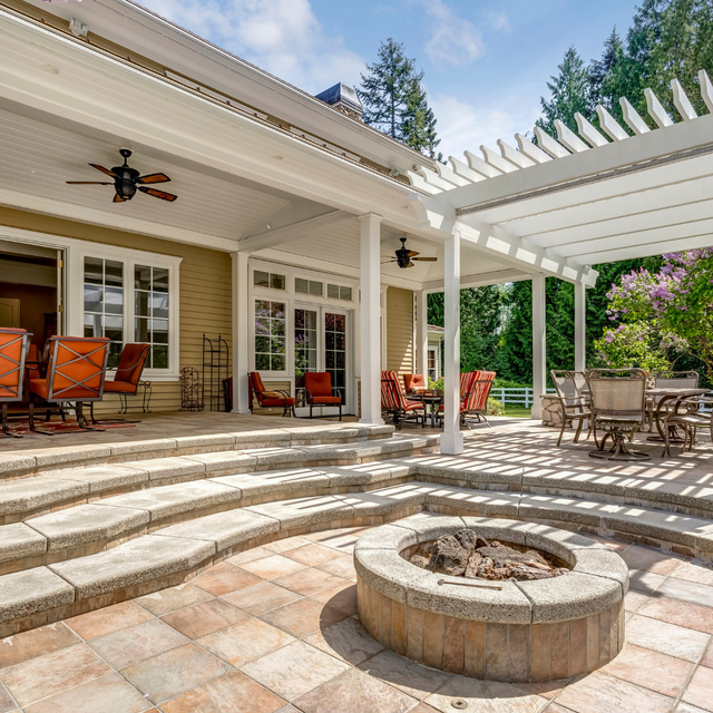 Spacious patio with stone steps, fire pit, pergola, and outdoor dining set beside a house.