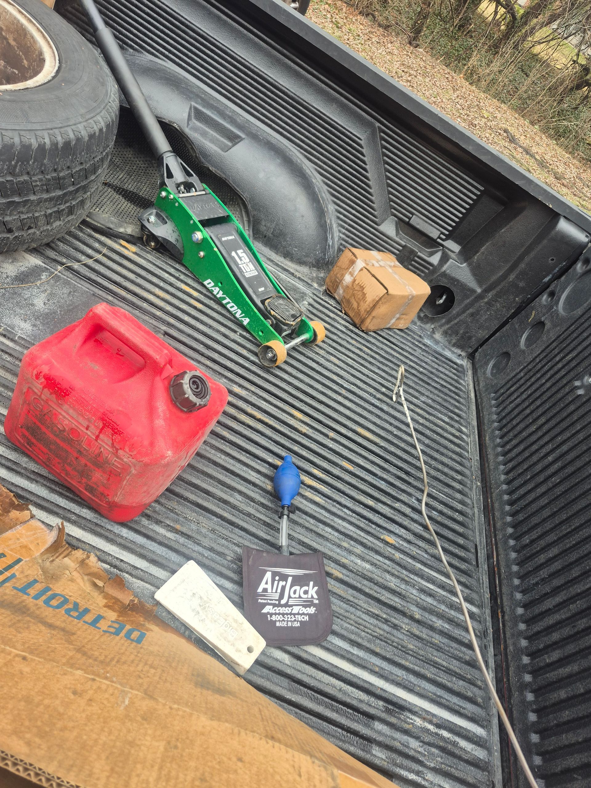Truck bed with a red fuel can, green jack, small box, and a key fob on a ribbed liner.