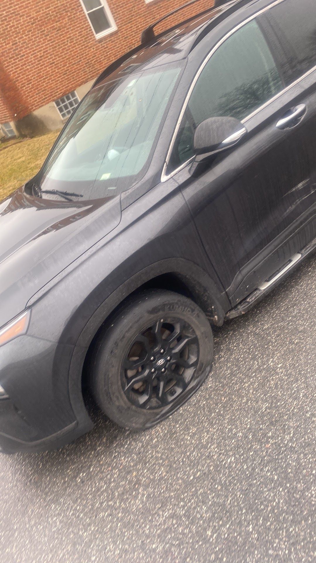 Dark gray SUV parked at an angle beside a brick building on a paved lot.