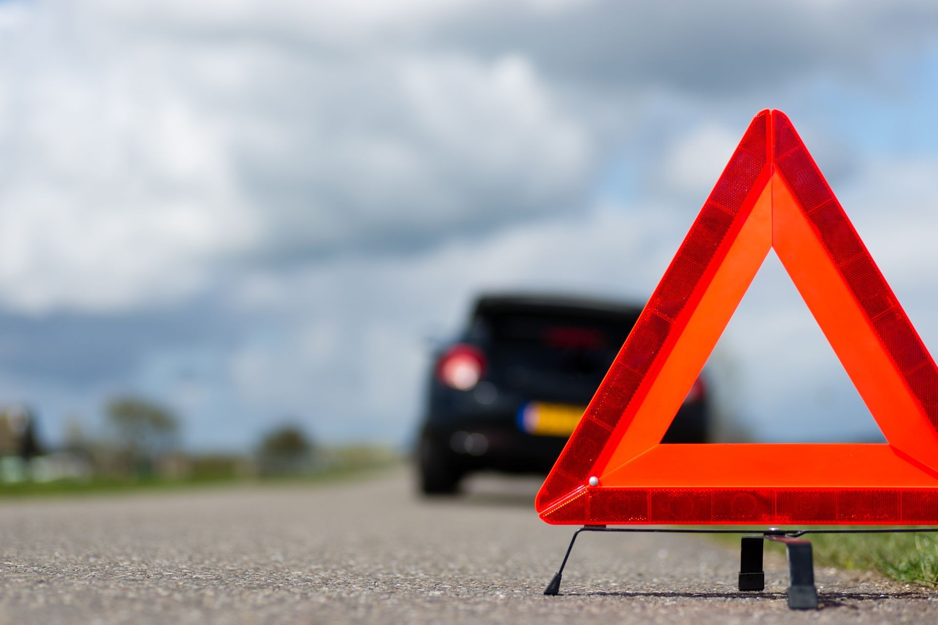 Red warning triangle on roadside with a blurred car in the background
