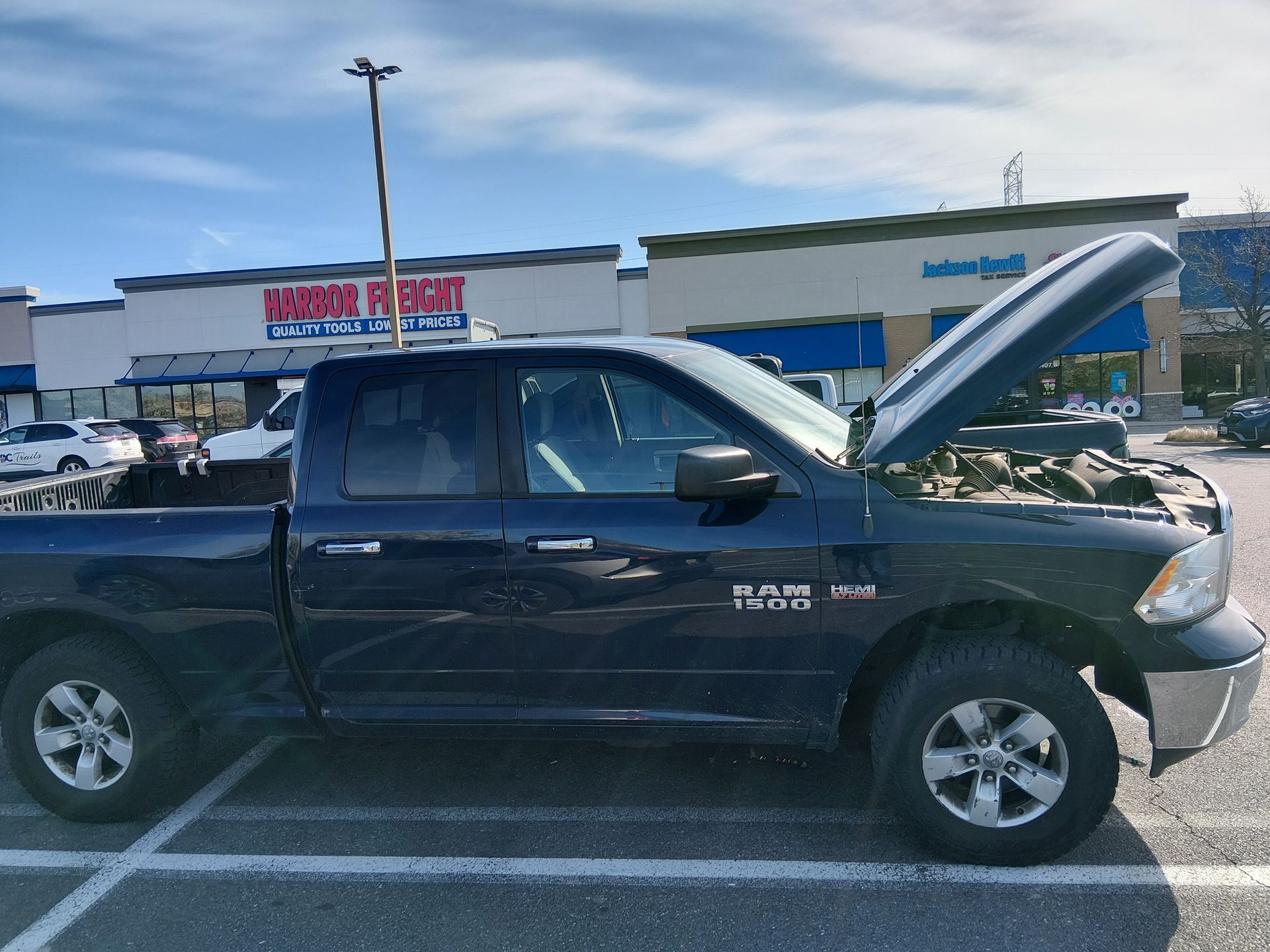 Black Toyota pickup with hood open in a parking lot outside a store.