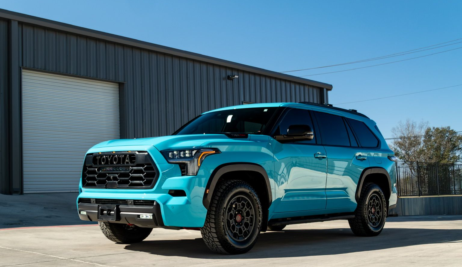 Turquoise SUV rear wheel with black off-road tire parked in sunlight