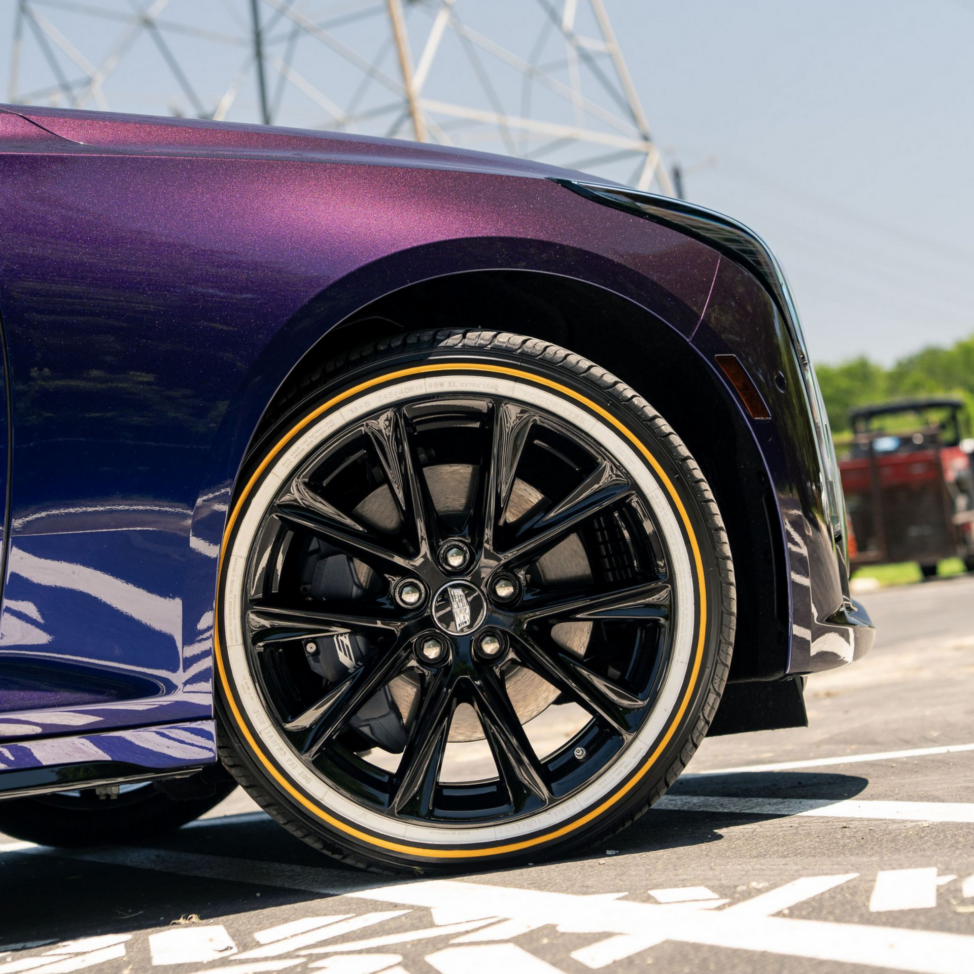 Close-up of a purple sports car’s front wheel with black rims and gold trim on pavement.