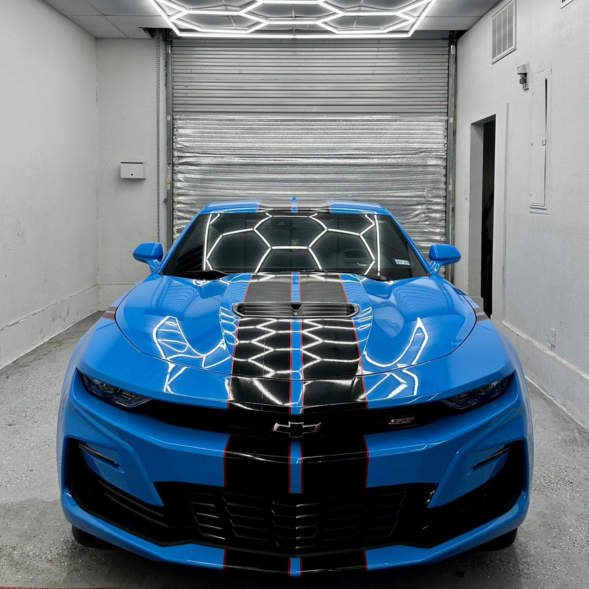 Blue sports car with black racing stripes in a garage-like showroom