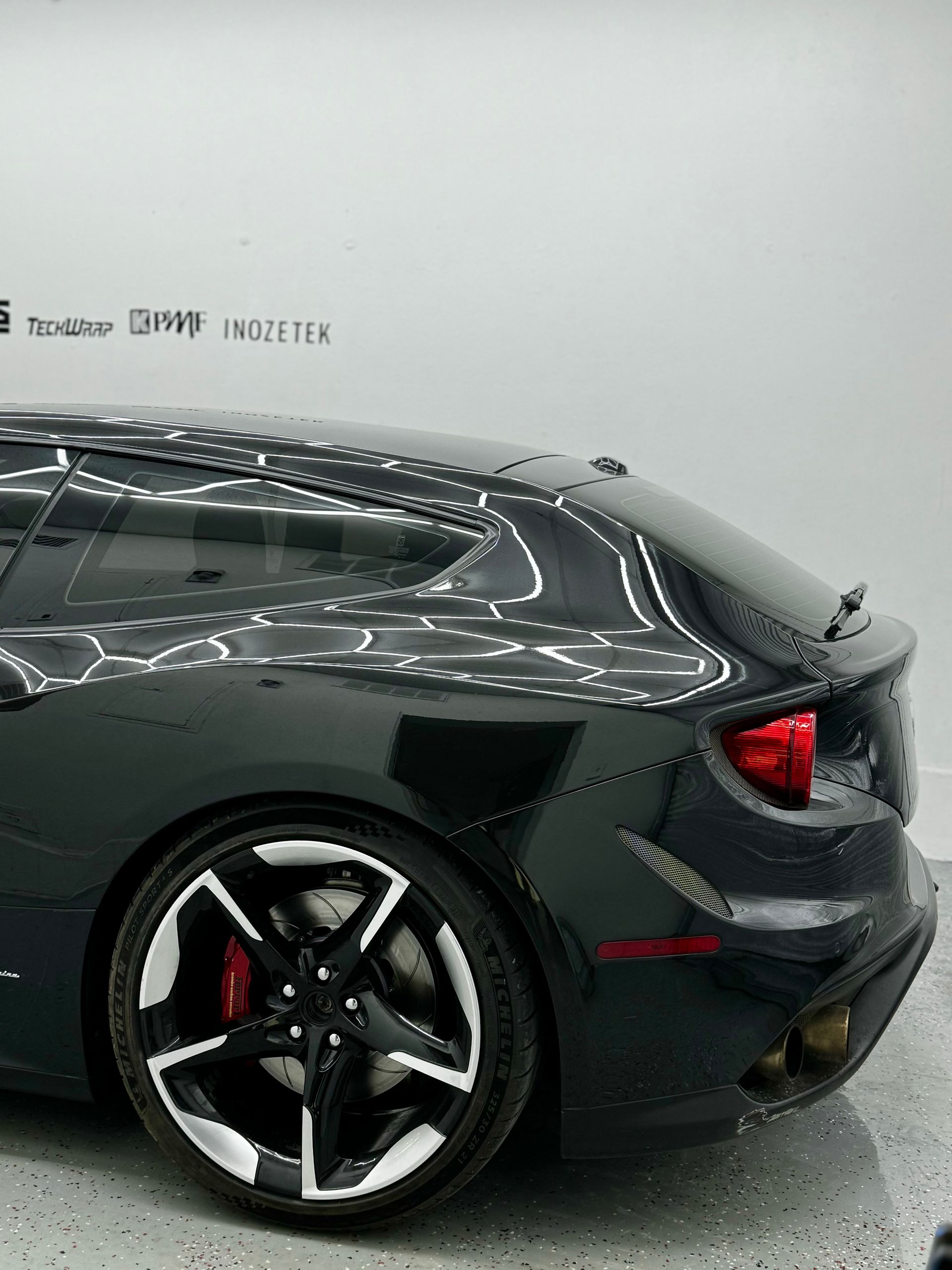 Black sports coupe in a showroom, rear side view with silver rims and red brake calipers