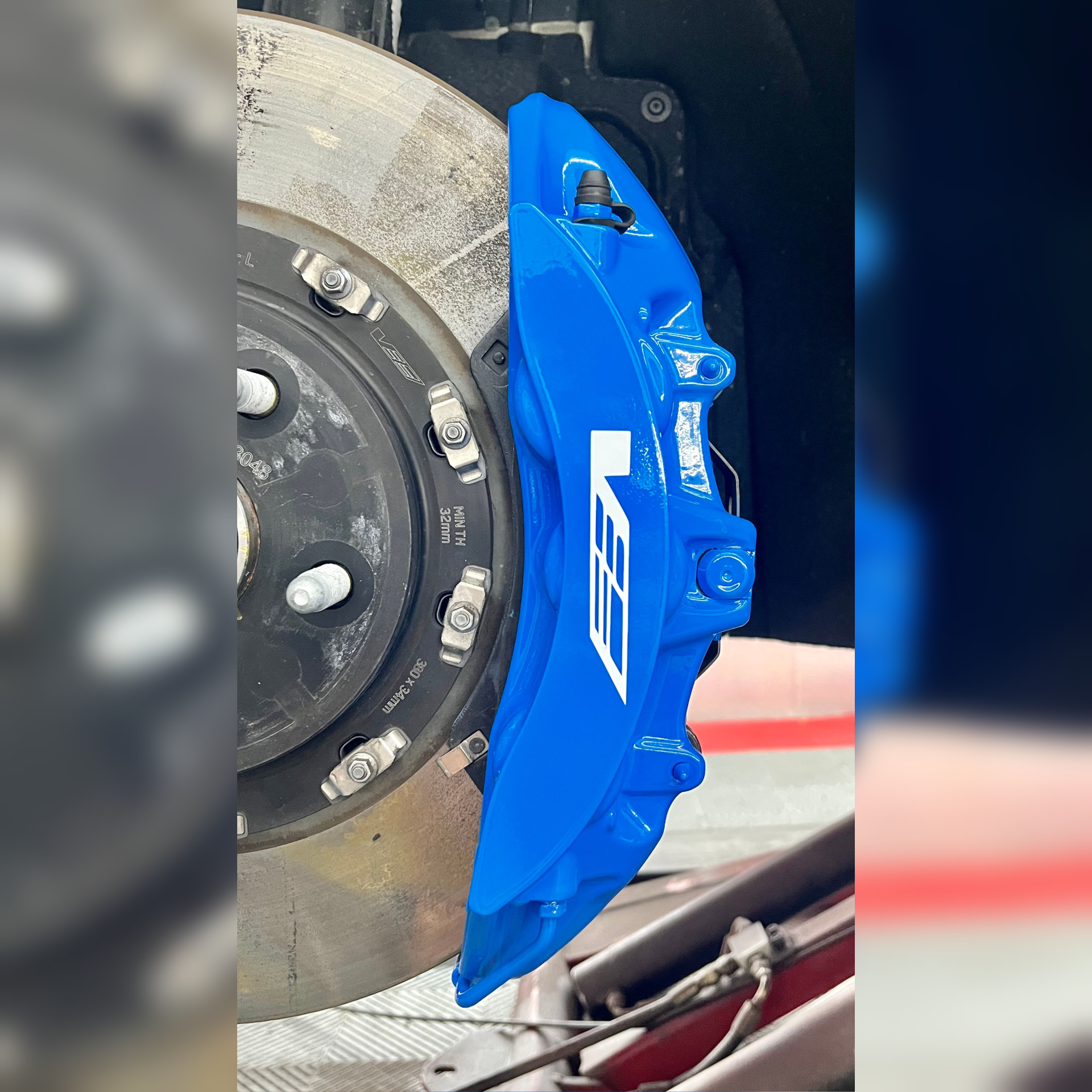 Blue brake caliper beside a car wheel and disc brake assembly